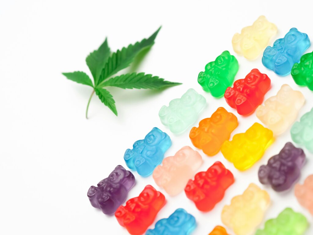 Vibrant gummy bears next to a cannabis leaf on a white background, symbolizing edible cannabis sweets.